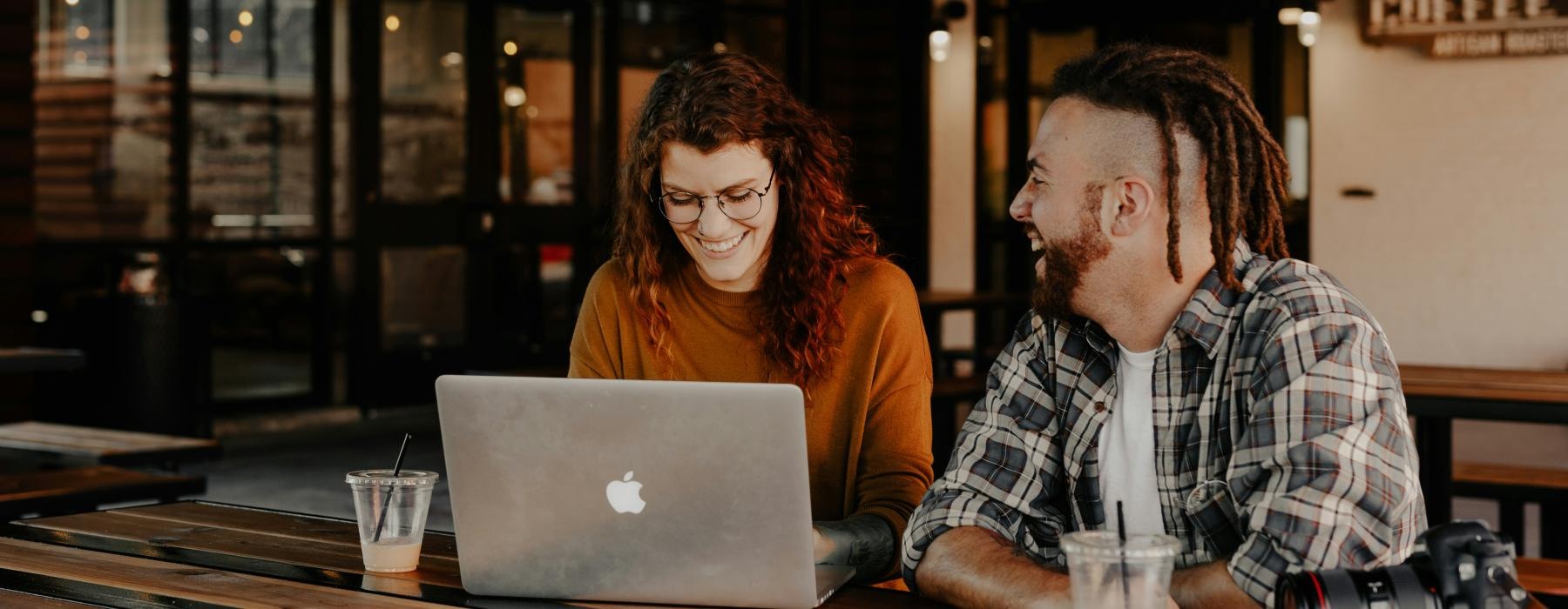 a man and woman sitting at a table looking at a laptop